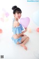 A woman sitting on the floor holding a pink heart shaped balloon.