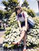 A girl in a school uniform sitting on a bush of flowers.