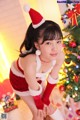 A woman in a santa outfit posing in front of a Christmas tree.