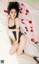 A woman in a black bodysuit laying on a bed with rose petals.