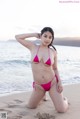 A woman in a pink bikini sitting on the beach.