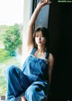 A woman in overalls leaning against a window.