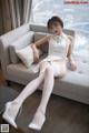 A woman sitting on a couch wearing white stockings and high heels.