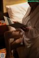 A woman in a bathrobe sitting on a bed reading a book.