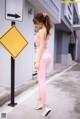 A woman in a pink sports bra top and pink leggings standing next to a parking sign.