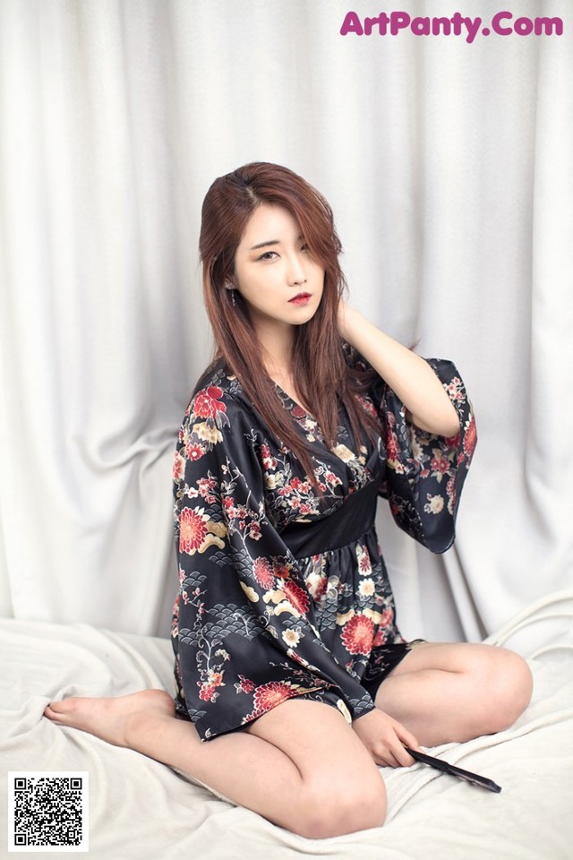 A woman sitting on a bed in a black robe.