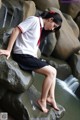 A woman in a school uniform sitting on a rock by a waterfall.