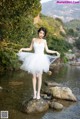 A woman in a white dress standing on a rock in the water.