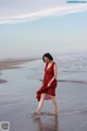 A woman in a red dress walking on the beach.