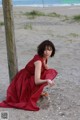 A woman in a red dress sitting on the beach.