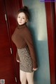 A woman in a brown turtle neck sweater and leopard print skirt.